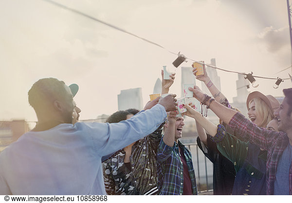 Enthusiastic young adult friends toasting cocktails at rooftop party