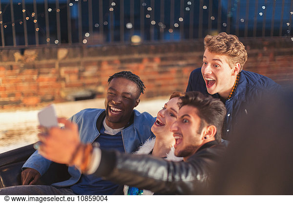 Enthusiastic young adults taking selfie at nighttime rooftop party