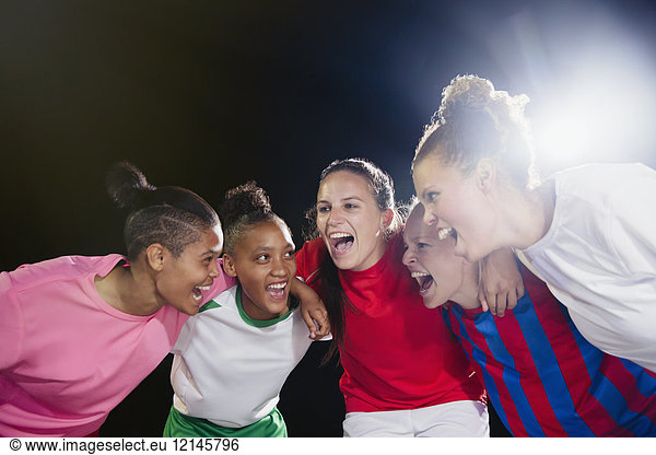 Enthusiastic young female soccer teammates celebrating  cheering in huddle