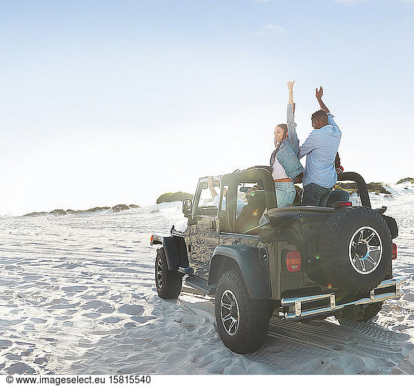 Enthusiastic young friends with arms raised  enjoying road trip on sunny beach