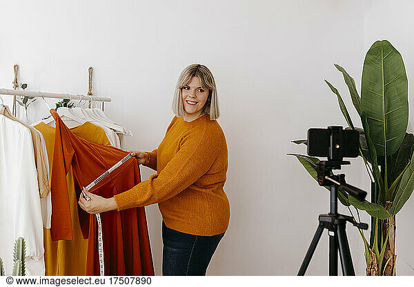 Entrepreneur measuring dress with tape measure doing video call at workshop
