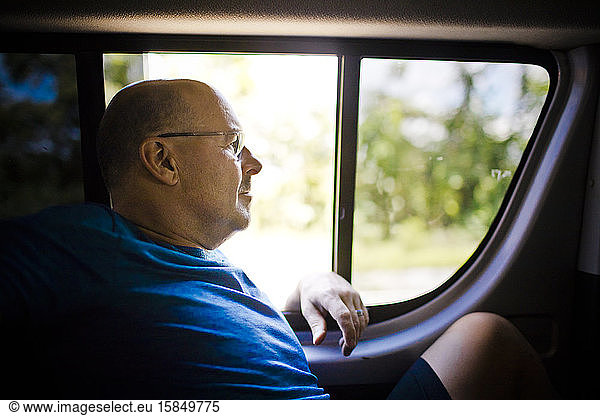 Entspannter Rentner sitzt hinten im Fahrzeug neben dem Fenster.