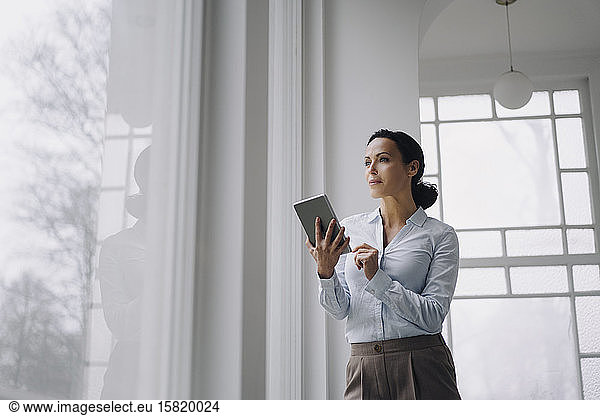 Erfolgreiche Geschäftsfrau  am Fenster stehend  mit digitalem Tablet
