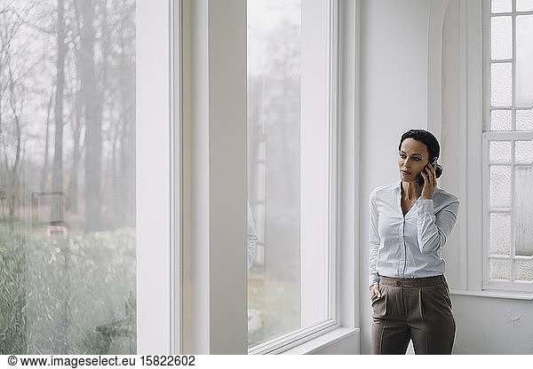 Erfolgreiche Geschäftsfrau  steht am Fenster und telefoniert