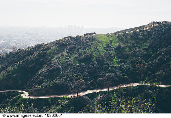 Erhöhte Ansicht einer kurvenreichen Straße und von Hügeln mit weit entfernter smogiger Stadtlandschaft  Los Angeles  Kalifornien  USA