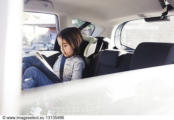 Ernsthafter Junge liest Buch  während er im Auto sitzt und durch das Fenster gesehen wird
