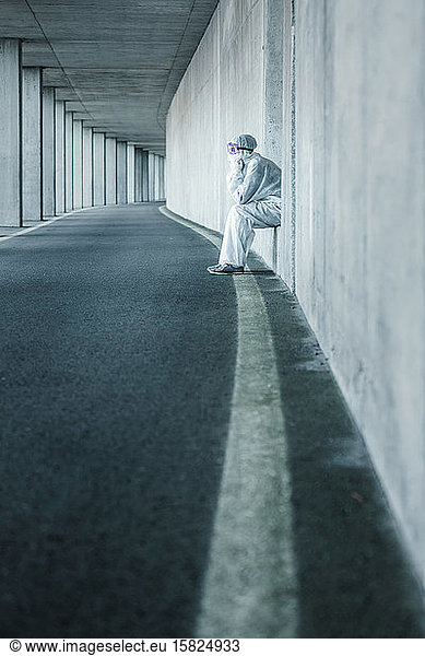 Erschöpfter Mann in Schutzkleidung sitzt in einer Nische einer Betonwand in einem Tunnel