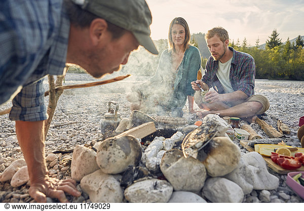 Erwachsene  die am Lagerfeuer sitzen  Essen zubereiten und Glut blasen