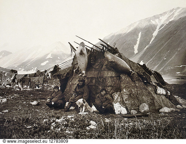 ESKIMO DWELLING  c1899. A group of three Inuits sitting in front of their house in the Arctic region with seal carcasses and furs hanging to dry. Photographed by Edward S. Curtis  c1899.