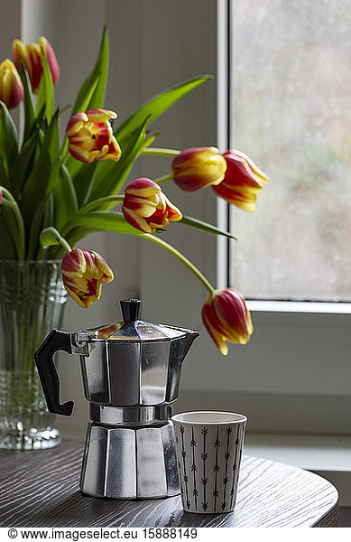 Espresso can and mug on a table with bouquet of tulips in the background