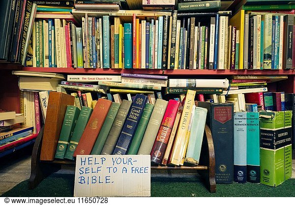 Estanteria llena de libros con un cartel escrito a mano 'HELP YOURSELF TO A FREE BIBLE'.Settle  North Yorkshire  Yorkshire Dales  Skipton  UK.