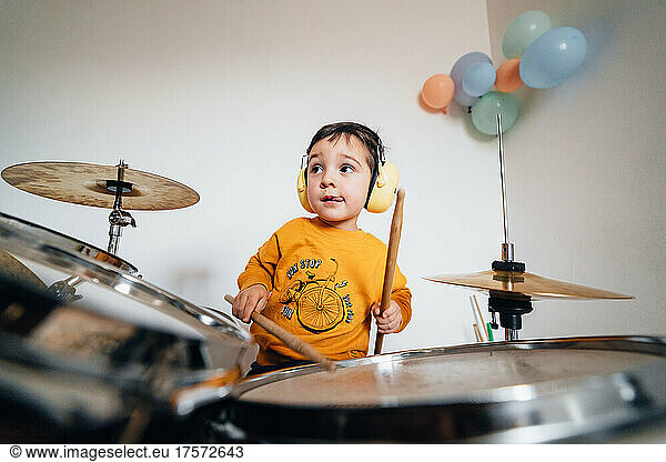 Estatic boy playing drums at home wearing safety headphones