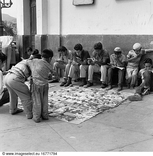 Ethnology:
Peru. Street scene in Lima: children and adolescents reading comics that have been sorted out and discarded as faulty stock by a bookstore. Photo  1965.