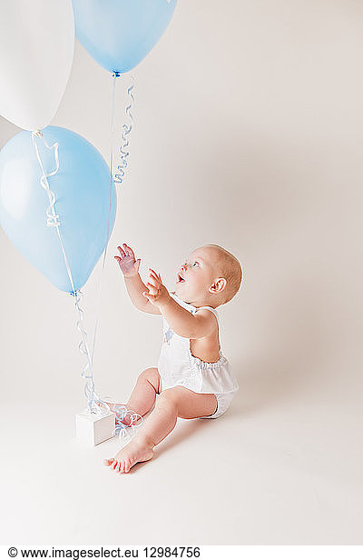 Excited baby boy with balloons and birthday present
