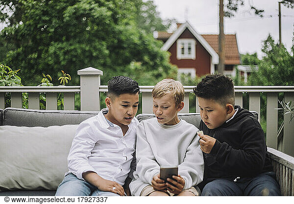 Excited boys sharing smart phone while sitting together on couch