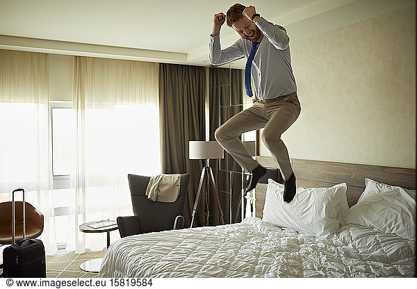 Excited businessman jumping on bed in hotel room