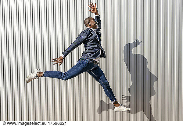 Excited businessman with hand raised jumping by white wall