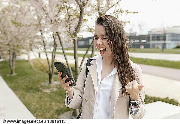 Excited businesswoman screaming with smart phone at footpath