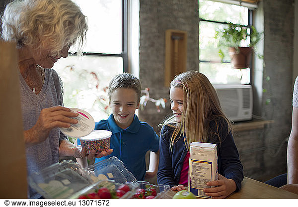Excited children looking at grandmother removing food in kitchen
