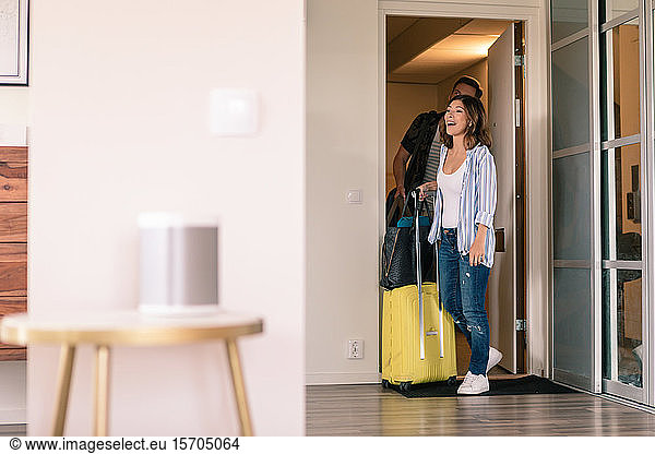 Excited couple with luggage entering in apartment during vacation