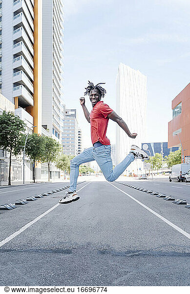 Excited ethnic man jumping on city street