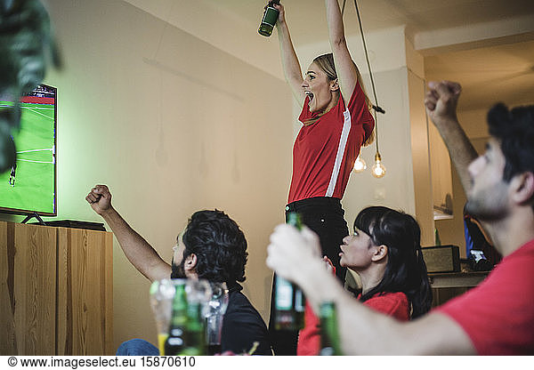Excited fans cheering for team while watching soccer match in living room