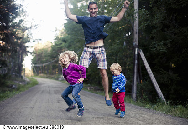 Excited father with two children jumping on country road