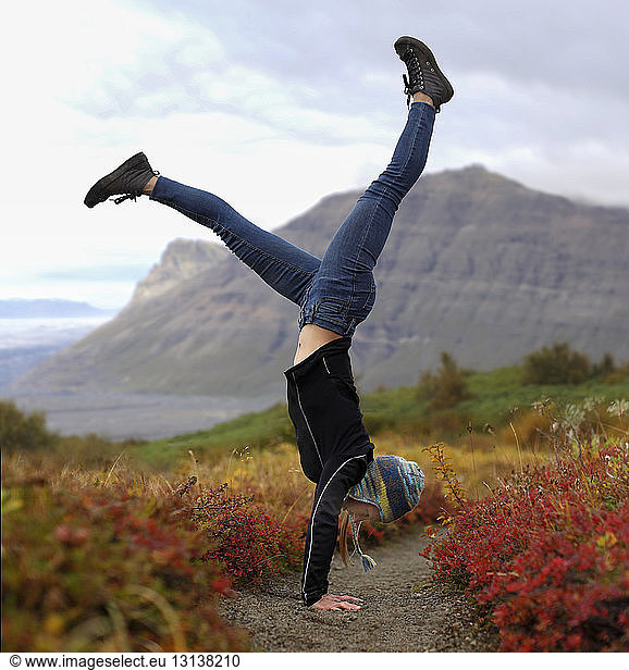 Excited female hiker doing handstand on field against mountains