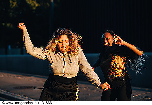 Excited friends dancing at skateboard park during sunset