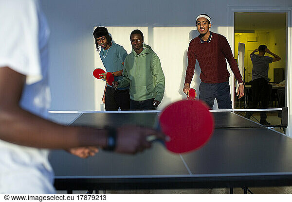 Excited friends playing table tennis in games room
