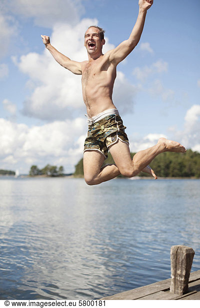 Excited mature man jumping into lake