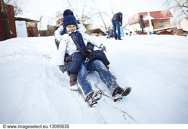 Excited mother and daughter tobogganing on snowy field