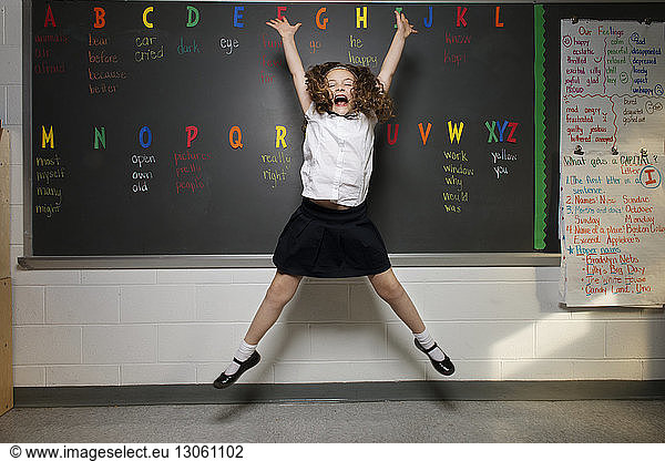Excited schoolgirl jumping against blackboard in classroom