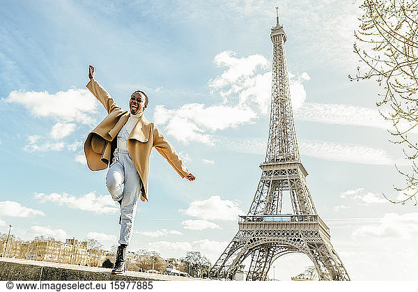 Excited woman jumping from retaining wall with Eiffel Tower in background  Paris  France