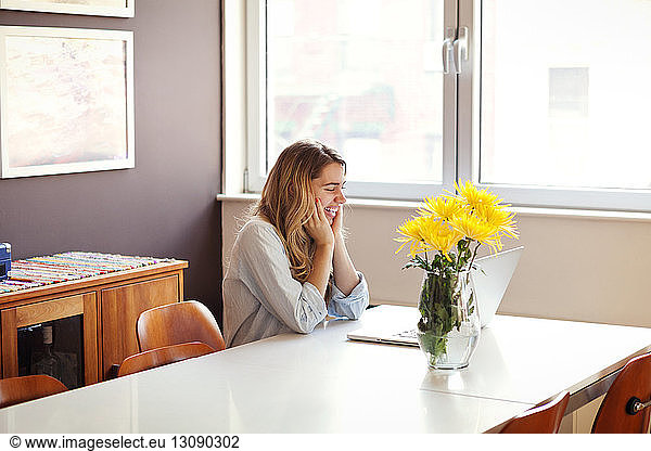 Excited woman looking at laptop by vase on table