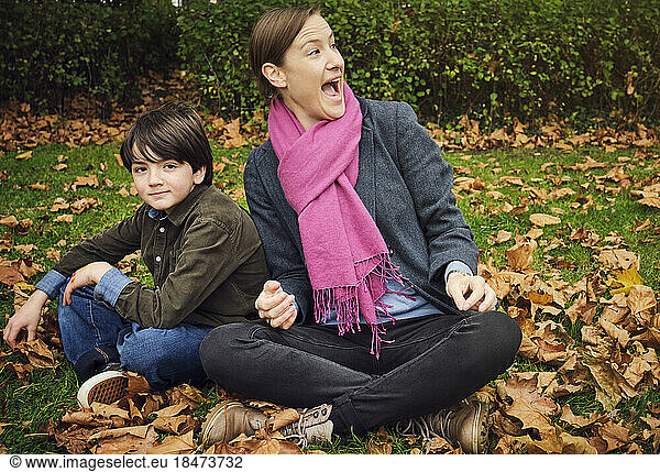 Excited woman sitting cross-legged by boy at park