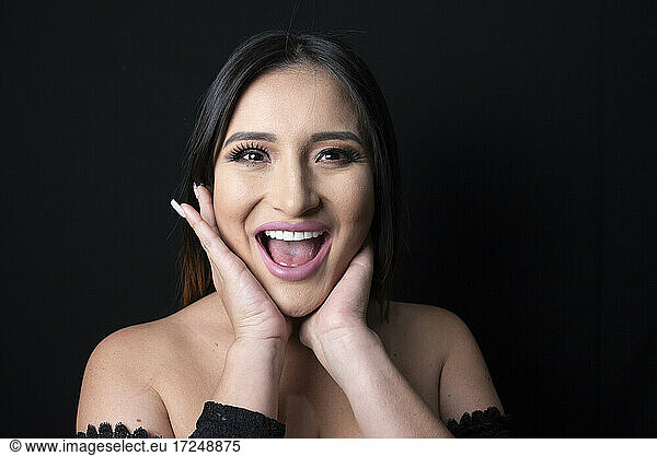 Excited woman touching cheeks against black background