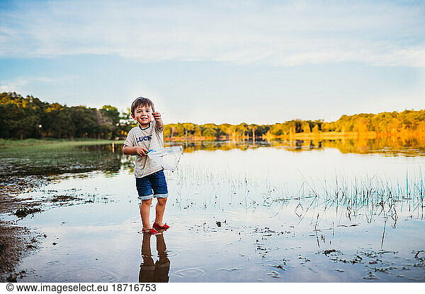 Excited young boy holding small fish he caught at the lake