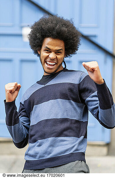Excited young man with curly hair gesturing while standing against wall