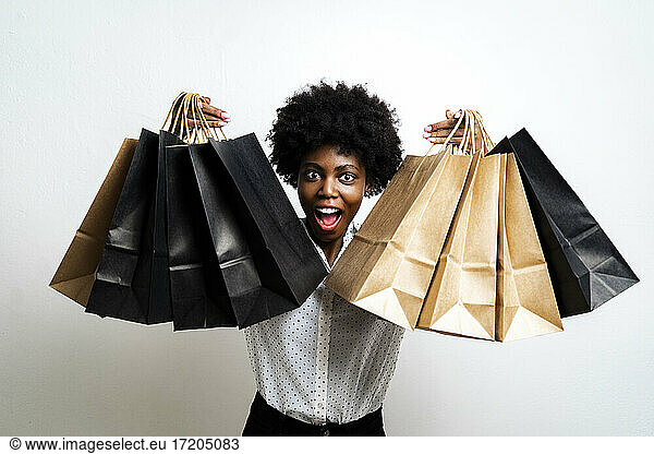 Excited young woman holding shopping bags while standing against white background
