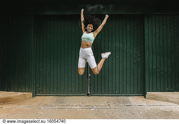 Excited young woman jumping against green metal door