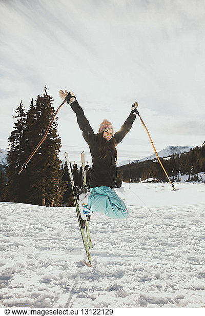 Excited young woman jumping while skiing on snowy field