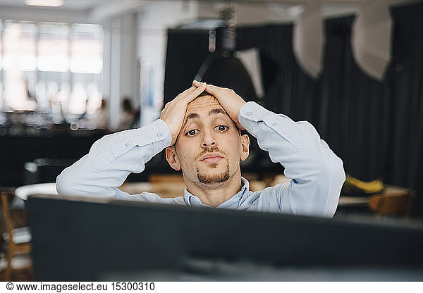 Exhausted computer programmer with head in hands looking at computer while working in office