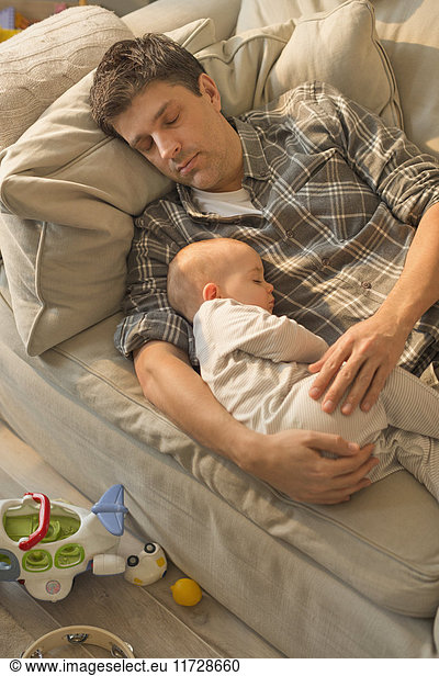Exhausted father and baby son sleeping on sofa