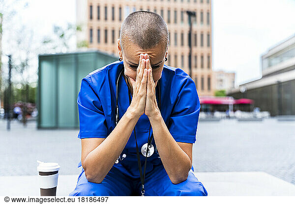 Exhausted healthcare worker with head in hands on footpath