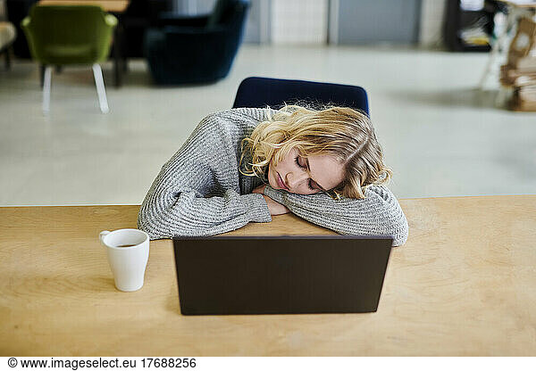 Exhausted young woman lying on desk in office