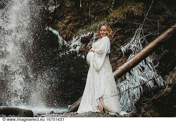Expecting woman looking down standing next to a waterfall in winter