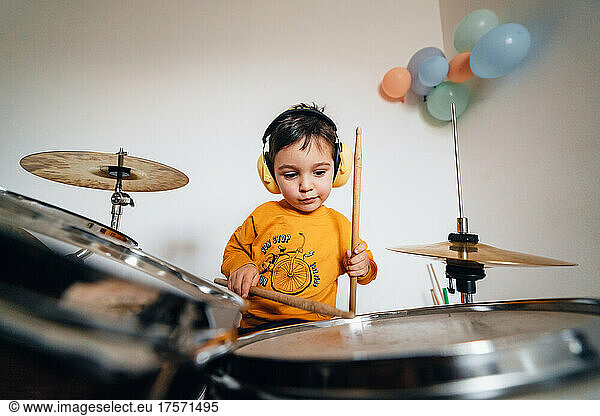Expresive kid playing drums with colored balloons on the wall