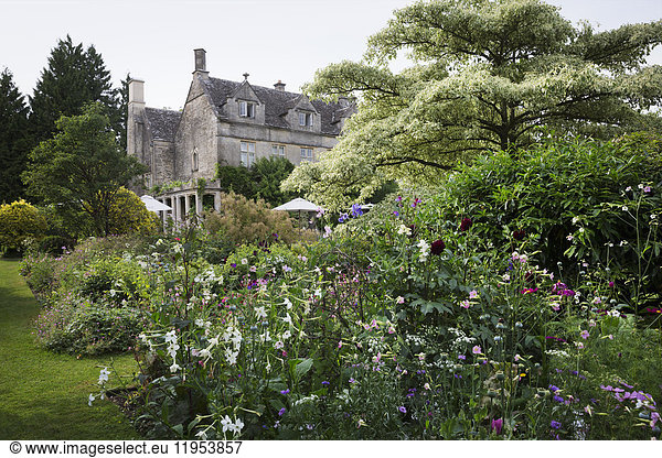 Exterior view of a 17th century country house from a garden with flower beds  shrubs and trees.