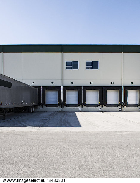 Exterior view of a warehouse loading dock with a truck trailer pulled up to one of the doors.